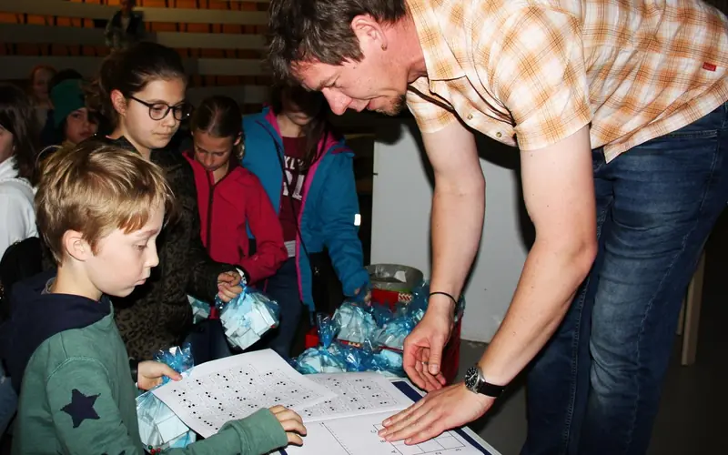 Markus Pfeil zeigt Kindern bei der Kinderuni der RWU ein Rätsel auf einem Blatt Papier